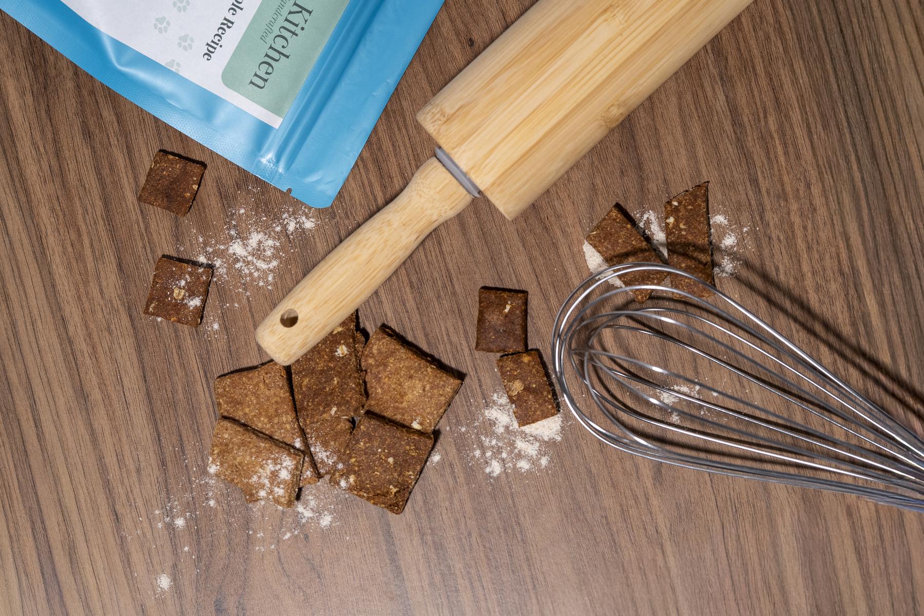 Peanut Butter and Apple Recipe treats on a wooden counter with a rolling pin, a whisk and a dusting of flour
